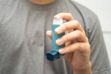 Astım ve kronik obstrüktif akciğer hastalığı COPD, Asyalı genç adam ölçülü doz solunum cihazı kullanıyor..