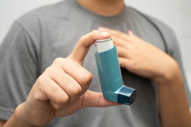 Astım ve kronik obstrüktif akciğer hastalığı COPD, Asyalı genç adam ölçülü doz solunum cihazı kullanıyor..