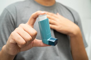 Astım ve kronik obstrüktif akciğer hastalığı COPD, Asyalı genç adam ölçülü doz solunum cihazı kullanıyor..