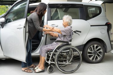 Caregiver help and support asian elderly woman sitting on wheelchair prepare get to her car to travel in holiday.