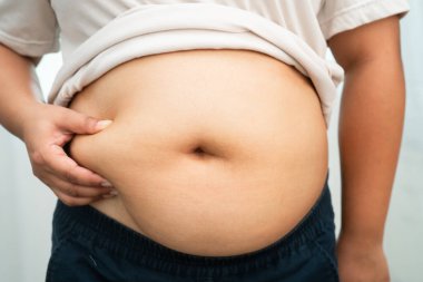 Asyalı kadın şişman göbeğini sıkmak için elini kullanıyor. Büyük boy aşırı kilolu ve obez..