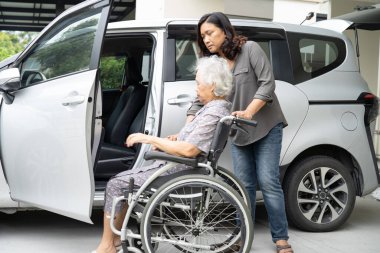 Caregiver help and support asian elderly woman sitting on wheelchair prepare get to her car to travel in holiday.