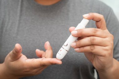 Evde parmak üzerinde dijital mızrakla kan şekeri seviyesini ölçmek için Asyalı kadın kendini test ediyor..