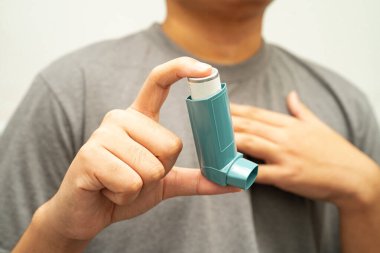 Astım ve kronik obstrüktif akciğer hastalığı COPD, Asyalı genç adam ölçülü doz solunum cihazı kullanıyor..