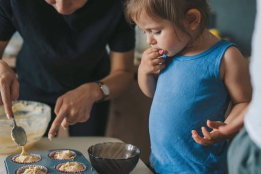 Pişirme tepsisi, anne ve kızının kek hamuruyla doldurduğu renkli kağıtlarla dolu, pişirmeye hazır. Çiğ hamur şeklinde çörekler. Tatlı yemek..