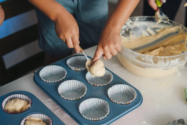 Close-up view of baking tins being filled with spoonfuls of raw dough to be placed in the oven. Friendly family, having fun, homemade baking, domestic life