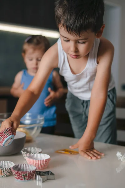 Caucasian boy selecting the baking tins to take to his mother to put the dough. Family cooking muffins, great design for any purposes. Happy family, childhood