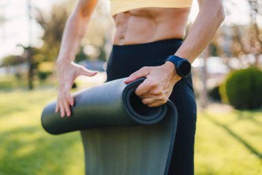 Akşamları kadın elleri egzersizden sonra yoga minderini çeviriyor. Yoga öğretmeni dışarıda. Antrenman egzersizi. Sağlıklı aktif yaşam tarzı. Fitness kadını. Yaz doğası.