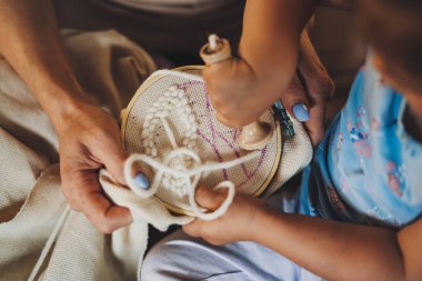 Kızına iğne ve iplikle nasıl nakış yapılacağını gösteren bir annenin elleriyle yakın plan. Aile eğitimi. İnsan kavramını seviyorum. Mutlu bir aile. Gülümsüyor