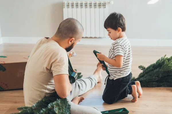 父亲和他的儿子站在房间里试图正确地爬上圣诞树的支架 圣诞节 冬天的概念 — 图库照片