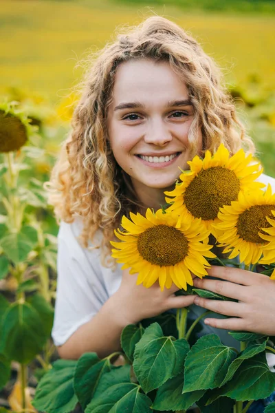 stock image A happy woman with curly-hair holding a bouquet of sunflowers in a field of sunflowers, smiling while looking at camera. Colorful landscape. Nature summer