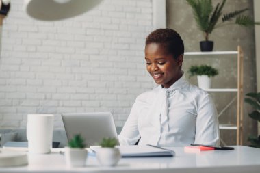 Laptop ekranına bakan, modern şirket ofisindeki bilgisayar klavyesinde yazan odaklanmış genç Afro-Amerikan iş kadını. İletişim ağı