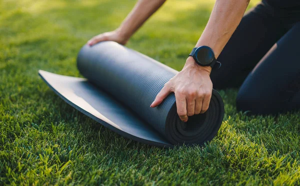 Unrolling a black yoga mat before a yoga lesson in the park. Close up picture. Healthy lifestyle, sport. Healthy activity. People lifestyle concept. Training