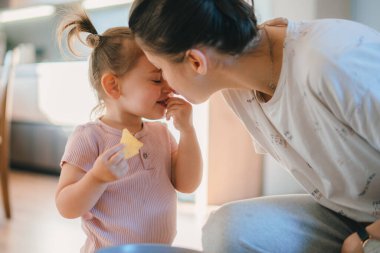 Küçük kız kurabiye yerken, beyaz bir annenin küçük kızını burnundan öpmesi. Ağzında kurabiye olan tatlı küçük bir kız. Çocuklar.