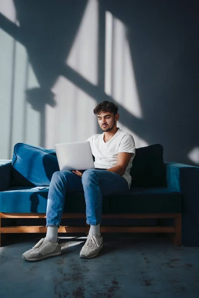 Jovem Bonito Sentado Sofá Azul Trabalhando Laptop Com Manchas Seus — Fotografia de Stock