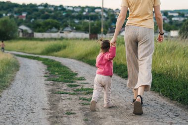 Bir annenin ve küçük kızının kırsalda yürüyüş yaparken görüntüsü. Uzayı kopyala Aktivite ilişkisi. Mutlu aile, çocukluk. Yaz doğası