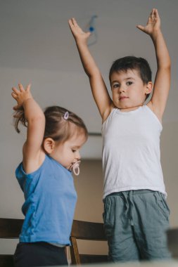 Oğlan onların öğle yemeğini beklerken mutfakta kız kardeşiyle oynuyor. Rahat çocuklar için ev kıyafetleri. Eğlenceli bir aile. Mutfağın içi..