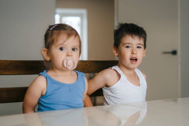 Neşeli, pozitif çocuklar masada oturup annelerinin açık mutfakta nasıl yemek yapılacağını öğrenmesini bekliyorlar. Halk yaşam tarzı, Anneler Günü konsepti..