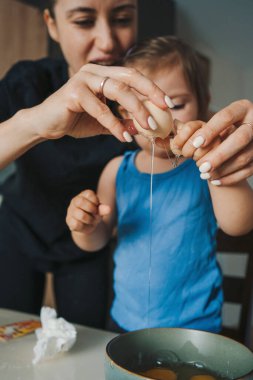 Anne kızının yumurtayı bir kasede başarıyla kırdığını öğreniyor ve kendinden çok memnun. Mutlu aile, çocukluk. Ebeveyn, çocuk. Eğlenceli bir aile. Tatlı.