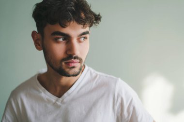 Yeşil arka planda duran yakışıklı genç adam doğal bir ifadeyle başka tarafa bakıyor. İzole edilmiş portre. Yeşil arka plan. Pozitif kişi. Moda modeli. Erkek