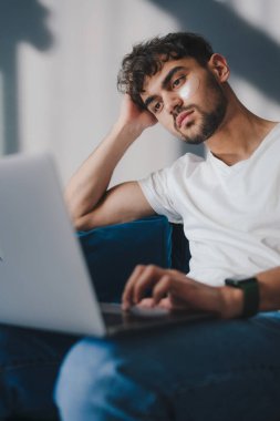 Gözlerinin altına yamalar yerleştirirken evdeki laptopta çalışan dalgın çocuk. Cilt bakımı. Kozmetoloji konsepti. Günlük çalışma