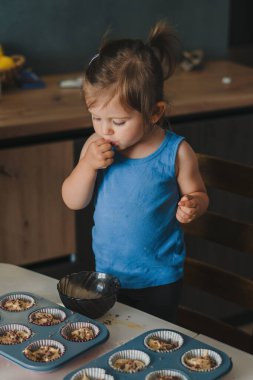 Şirin, küçük, mutlu bir kız bebek ev mutfağında yaban mersinli kek dekore ediyor. Komik, sağlıklı çocuk eğleniyor, tatlı hamuru tadıyor. Küçük