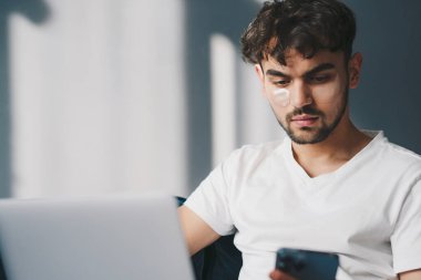 Evdeki bir kanepede oturan çekici genç adam dizüstü bilgisayarında yazarken cep telefonu kullanıyor. İş adamları iletişim kuruyor. İnternet iletişimi