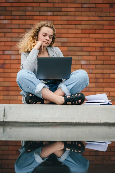 Kudrnatá Zamyšlená Studentka Sedící Používající Notebook Cihlovém Pozadí Univerzitního Kampusu — Stock fotografie