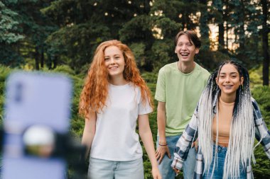 Parkta telefonla çevrimiçi video yayınlarken dans eden üç genç yaratıcı. Sosyal medya sorunu ağ uygulaması. Yayınlanan video. Cep telefonu