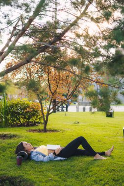 Çekici genç bir kadın elinde kitapla dışarıda yeşil çimlerin üzerinde dinleniyor. Güzellik portresi. Doğa yazı. Yeşil doğa. Doğal güzellik..