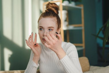 Güzel genç bayan kanepede oturuyor, güzellik prosedürünün tadını çıkarıyor, beyaz bir yüz maskesi takıyor. Güzellik tedavisi. Doğal güzellik. Kadın yüzü