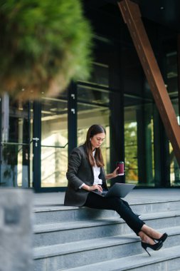 Ofis binasının yanında oturan kadın uzmana yoğunlaşın, açık havada şehrin kablosuz bağlantısıyla uzaktan kumanda edin. Veri analizi İş analizi.