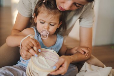 Beyaz bir anne küçük kızına örgü örmeyi öğretiyor. Elinde iğneler ve ipliklerle yerde oturuyor. Hobi ve eğlence. İnce motor beceriler kavramını geliştirmek için etkinlik