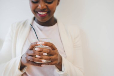 Kafeteryada elinde bir bardak kahveyle oturan serbest çalışan Afro bir kadın. Kafeteryada dinleniyor, öğle yemeği için arkadaşlarını bekliyor. Mutlu siyah kız