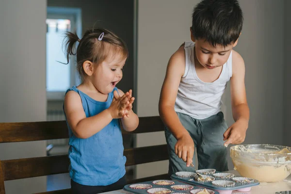 两个白人小孩在厨房做蛋糕 给杯子里的蛋糕填饱肚子 孩子们用生面团填松饼 — 图库照片