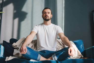 Deniztarağı delikanlısı evdeki yüz bakımı sırasında kanepede meditasyon yapıyor ve dinleniyor. İşten sonra ara. Gözlerini kapat ve derin bir nefes al yogayla huzur içinde.