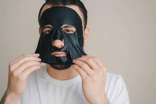 Πορτραίτο Ενός Νεαρού Άντρα Ξεφλουδίζει Μια Μαύρη Μάσκα Προσώπου Απομονωμένη — Φωτογραφία Αρχείου