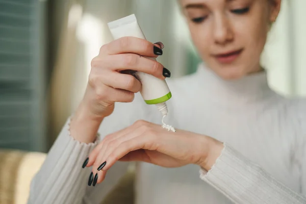 Stock image Young woman at home, putting moisturizer white cream on her hands. Skin body cream moisturizing lotion, routine in the morning. Beauty care, skin problem