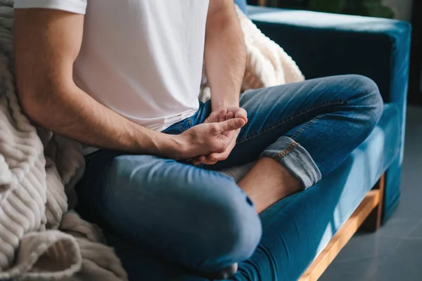Close-up view of mans legs crossed on sofa and hands crossed in meditation position. Health care. Body care.