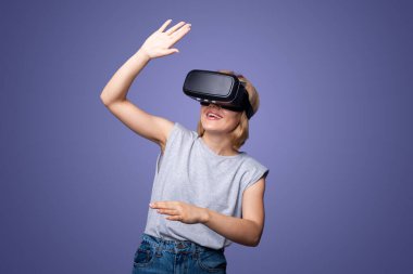 Modern VR gözlüklü kadın mor arka planda izole edilmiş sanal gerçeklik deneyimi yaşıyor. Gelişmiş gerçeklik oyunu, geleceğin teknolojisi. Gelecekçi yaşam tarzı.