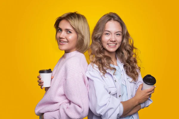 两个金发女郎背靠背地站在那里 手里拿着一杯咖啡 看着摄像机 快乐的女朋友在一起 — 图库照片