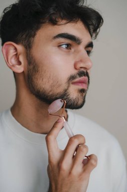 Yeşim taşıyla masaj yapan yakışıklı bir adam. Lüks kaplıca tedavisi için yüz masajı ile kozmetik, sağlık ve yeşim taşı yüz masajı