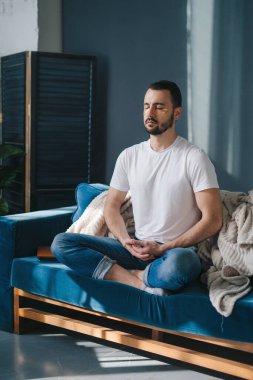 Kanepede bacak bacak bacak üstüne atmış bir adam oturma odasında meditasyon yapıyor. Gelişimsel sağlık ve beyin gelişimini destekleme kavramı.