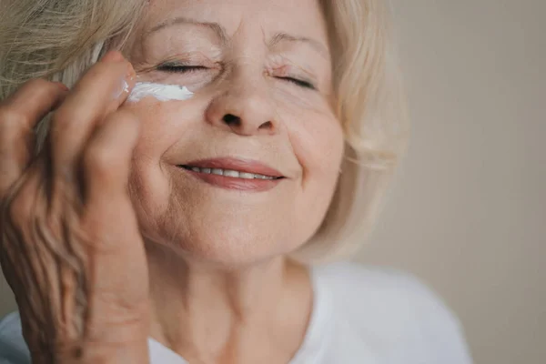 Happy mature woman woman applying anti-aging lotion to remove dark circles under eyes. Makeup product. Smile face.