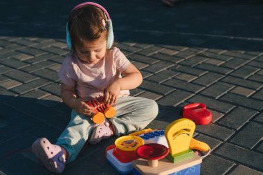 Gün batımında bahçede oturan küçük kız yeteneklerini geliştiren bir sürü oyuncakla oynuyor. Doğa yazı. Eğitici oyuncaklar. Mutlu aile.