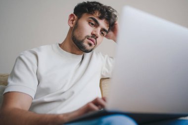 Webinars izleyen genç bir öğrenci, evinde kanepede otururken bilgisayarla uzaktan öğreniyor. İnsanların yaşam tarzı. Konforlu daire.