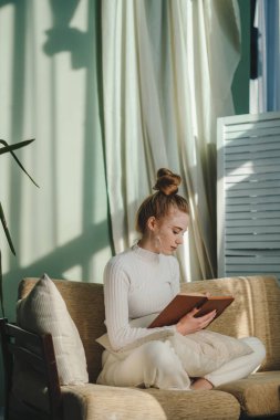 Güzel genç bayan kanepede oturuyor, evde güzellik kuralları sırasında kitap okurken eğleniyor. Kız yüz tedavisi. Terapi tedavisi, güzellik