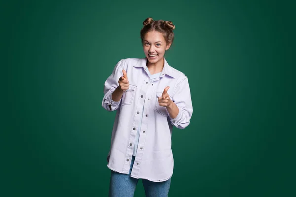 Pretty woman making finger gun gesture at camera, expressesing choice isolated over green background. Says you are chosen. Happiness concept. Positive person.