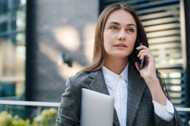 İş kadını elinde dizüstü bilgisayarla caddede yürüyen cep telefonuyla konuşuyor, acele et. Yürüyorum, şehirde caddeye çıkıyorum. Cep telefonu