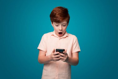 Kafkasyalı bir çocuk telefonun ekranına bakıyor. Yanlışlıkla utancından şoka girmiş. İnternet teknolojisi. İş, yaşam tarzı konsepti. Komik görünüşlü insan.